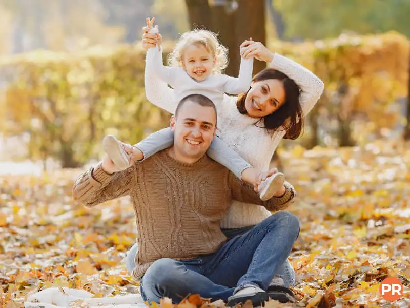 Family sitting in leaves and smiling.