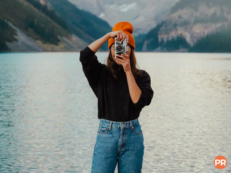 Photographer taking a picture near a lake with mountains in the background.